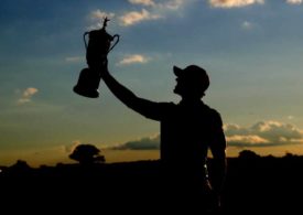 Im Sonnenuntergang die Silhouette eines Golfers der einen Pokal hochstemmt