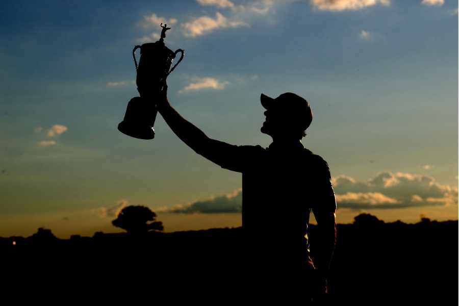 Im Sonnenuntergang die Silhouette eines Golfers der einen Pokal hochstemmt