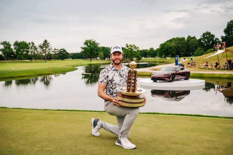 Ein Golfer mit Pokal vor einem Wasserhinderniss und ein Porsche im Hintergrund