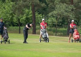 Vier Golfer stehen um ein Golfloch mitder Fahne des Golfclubs, zwei der Golfe geben sich die Faust