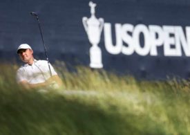 Scottie Scheffler im hohen Gras, im Hintergrund das Logo der U.S. Open
