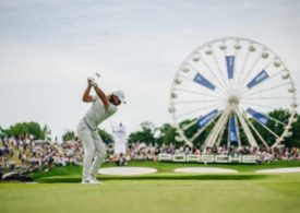 Ein Golfer schlägt ab, im Hintergrund ein Riesenrad