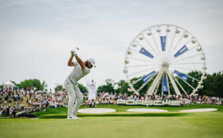 Ein Golfer schlägt ab, im Hintergrund ein Riesenrad