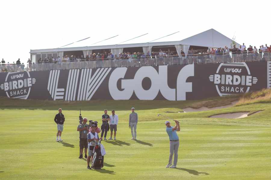 Ein Golfer mit Caddie und Kamerateam vor einer Zuschauer-Tribüne