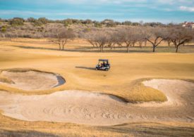 Ein Golfcart fährt auf einem ausgetrockneten Platz mit Sandbunkern