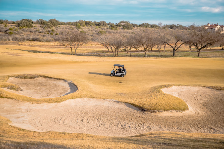 Ein Golfcart fährt auf einem ausgetrockneten Platz mit Sandbunkern