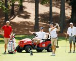 Ein Golfer beim Abschlag, drei Männer schauen zu