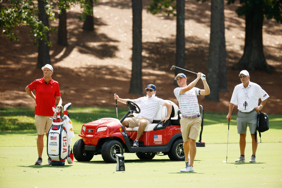 Ein Golfer beim Abschlag, drei Männer schauen zu