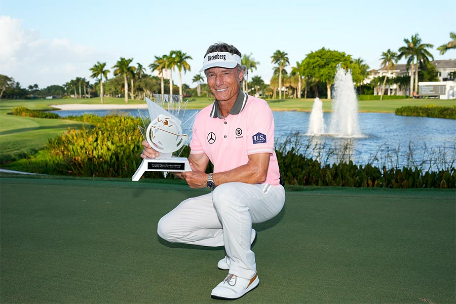 Bernhard Langer hockt vor einem Teich mit einem Pokal in seinen Händen