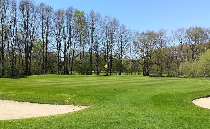 Ein Golfplatz mit zwei Sandgruben links und rechts und in der Mitte steht eine gelbe Fahne