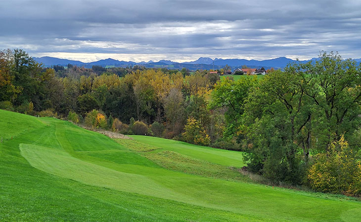 Ein hügeliger Golfplatz, im Hintergrund Berge