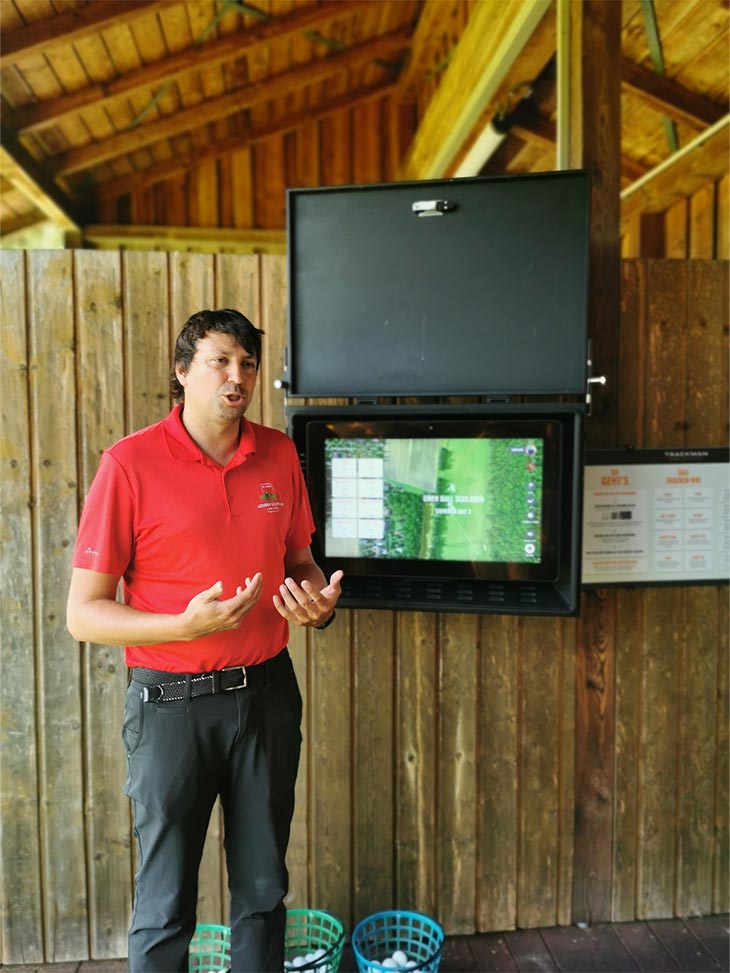 Ein Mann im rotem Poloshirt steht neben einem Bildschirm