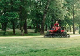 Ein Greenkeeper fährt mit einem Rasenmäher-Traktor über den Golfplatz