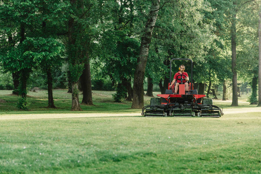 Ein Greenkeeper fährt mit einem Rasenmäher-Traktor über den Golfplatz