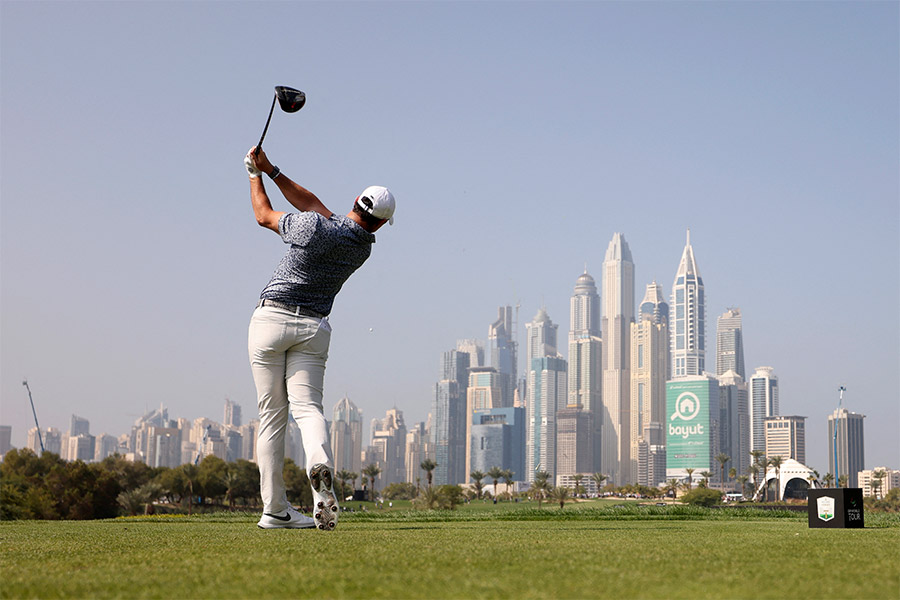 Ein Golfspieler schlägt ein Golfball mit seinem Schläger und im Hintergrund sieht man Wolkenkratzer