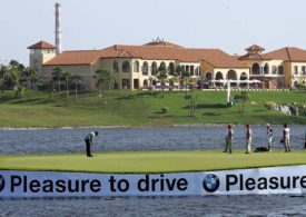 Eine Golfwiese mitten im Wasser und im Hintergrund sieht man ein großes Gebäude