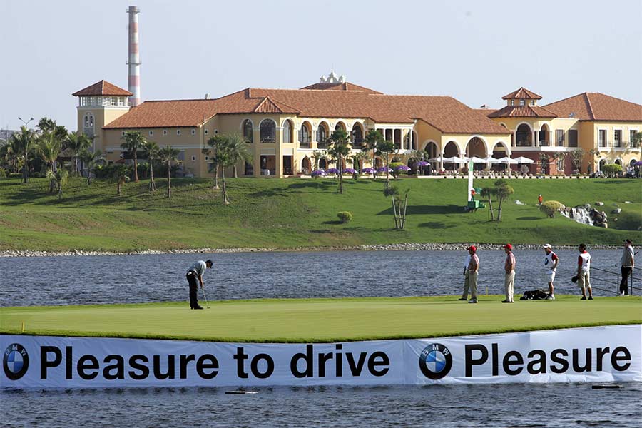 Eine Golfwiese mitten im Wasser und im Hintergrund sieht man ein großes Gebäude