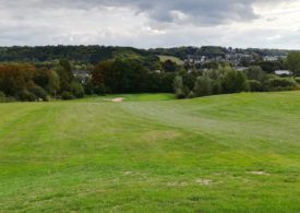 Grüne Hügel auf einem Golfplatz, hinten rechts eine Siedlund