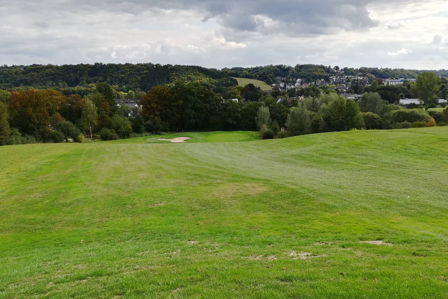 Grüne Hügel auf einem Golfplatz, hinten rechts eine Siedlund