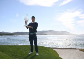 Ein Golfer präsentiert den Pokal, vor dem Meer stehend