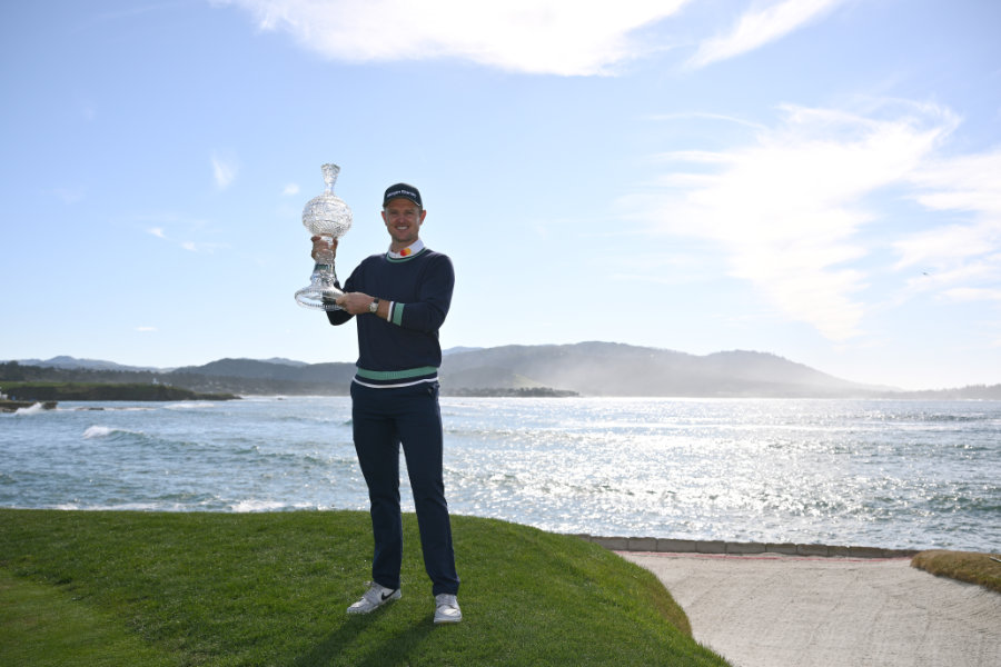 Ein Golfer präsentiert den Pokal, vor dem Meer stehend
