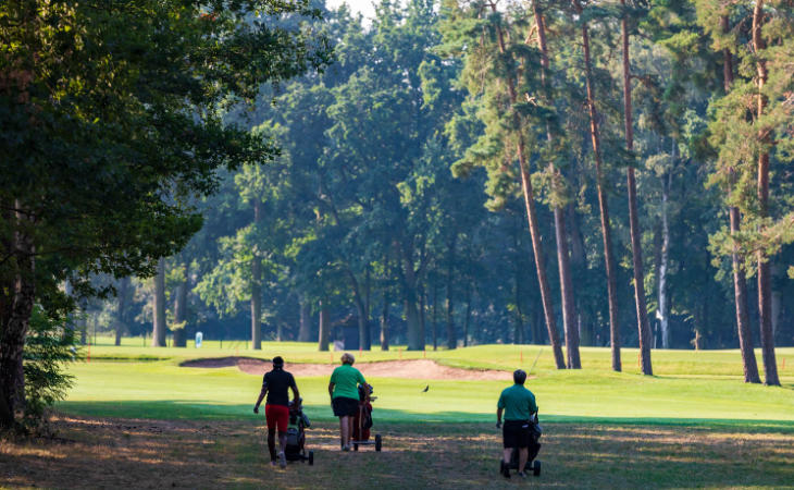 Golfer schieben ihre Trolleys über einen Golfplatz