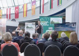 Michael Torres spricht vor Publikum auf der Bühne einer Golfmesse