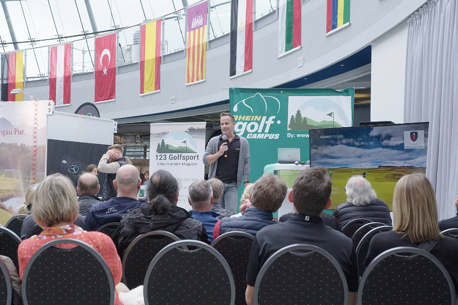 Michael Torres spricht vor Publikum auf der Bühne einer Golfmesse