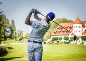 Rückansicht eines Golfers beim Abschlag, vor ihm ein Golfhotel