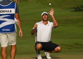Ein Golfer hockt auf der Wiese und wirft einen Golfball hoch in die Luft