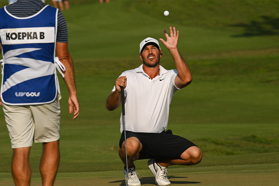 Ein Golfer hockt auf der Wiese und wirft einen Golfball hoch in die Luft