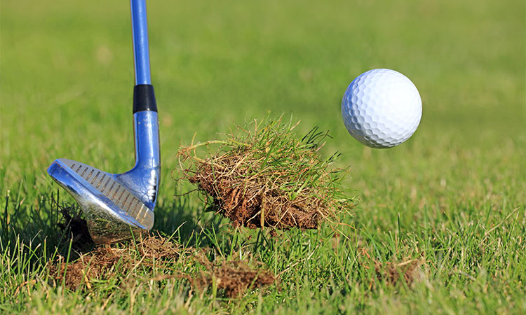 Ein Golfschläger schlägt ein Golfball in die Luft und dabei wird ein Stück Rasen mit gerissen