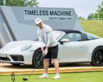 Der Golfspieler Nick Bachem steht mit seinem Golfschläger vor einem grauen Porsche