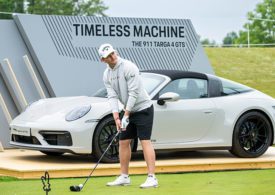 Der Golfspieler Nick Bachem steht mit seinem Golfschläger vor einem grauen Porsche