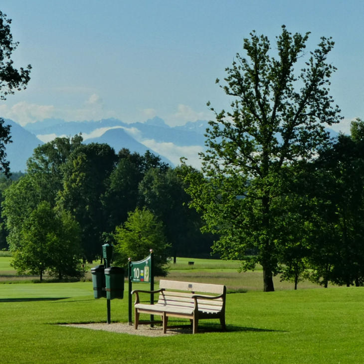 Eine Sitzbank auf einem Golfplatz, im Hintergrund Berge
