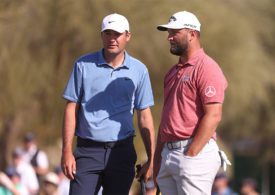 Die Golfspieler Scottie Scheffler und Jon Rahm stehen neben einander und halten beide ein Golfschläger in der Hand