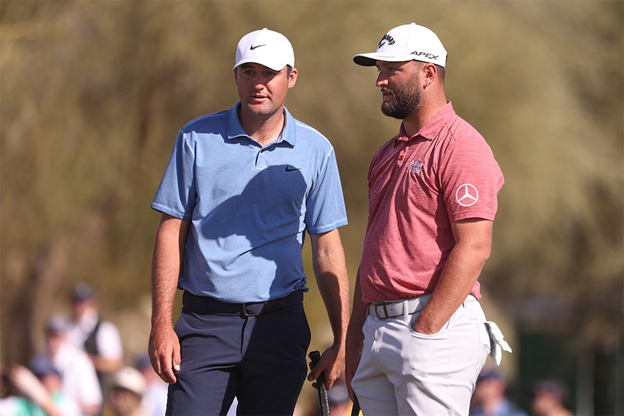 Die Golfspieler Scottie Scheffler und Jon Rahm stehen neben einander und halten beide ein Golfschläger in der Hand