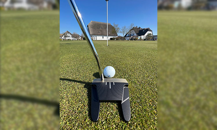 Ein Bild von dem Golfschläger Smithworks rb3 der einen Golfball berührt und im Hintergrund sieht man das Clubhause von Jens Albrecht