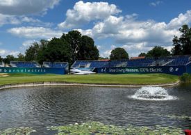 Ein Teich mit einer Wasserfontäne und im Hintergrund ist ein Golfplatz mit einer Tribüne