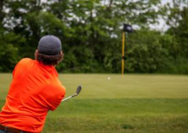 Ein Golfer im roten Poloshirt chippt den Ball aufs Grün