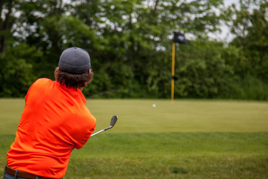 Ein Golfer im roten Poloshirt chippt den Ball aufs Grün