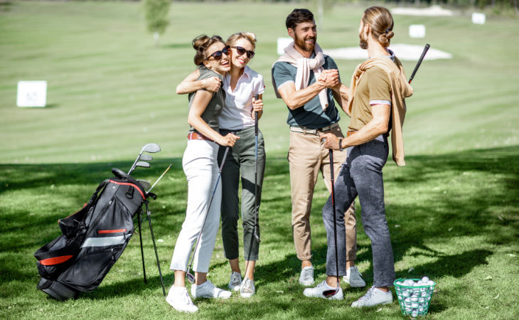 Zwei junge Männer und zwei junge Frauen begrüßen sich herzlich auf einem Golfplatz