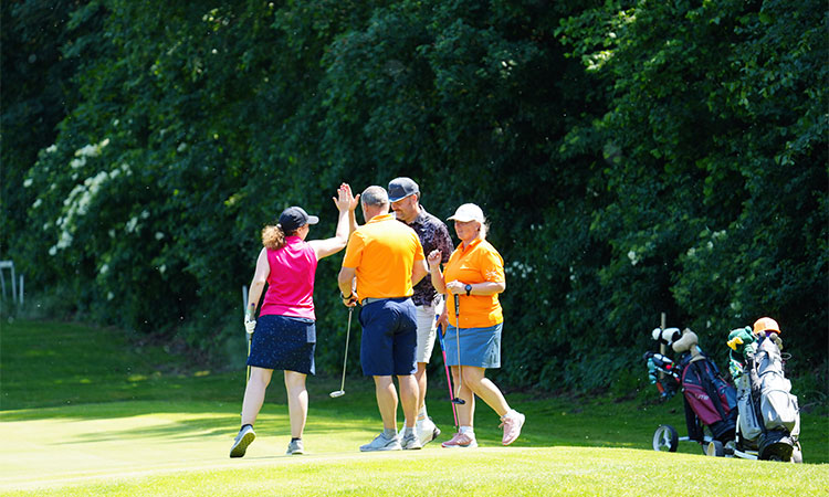 Vier Golfspieler stehen zusammen auf einer Golfwiese und rechts sieht man ihre Golfer Ausrüstung