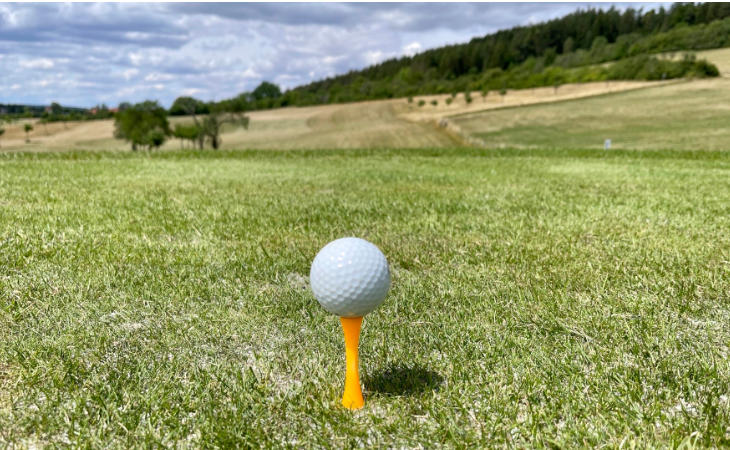 Nahaufnahme eines Golfballs auf einem Tee, dahinter ein Golfplatz