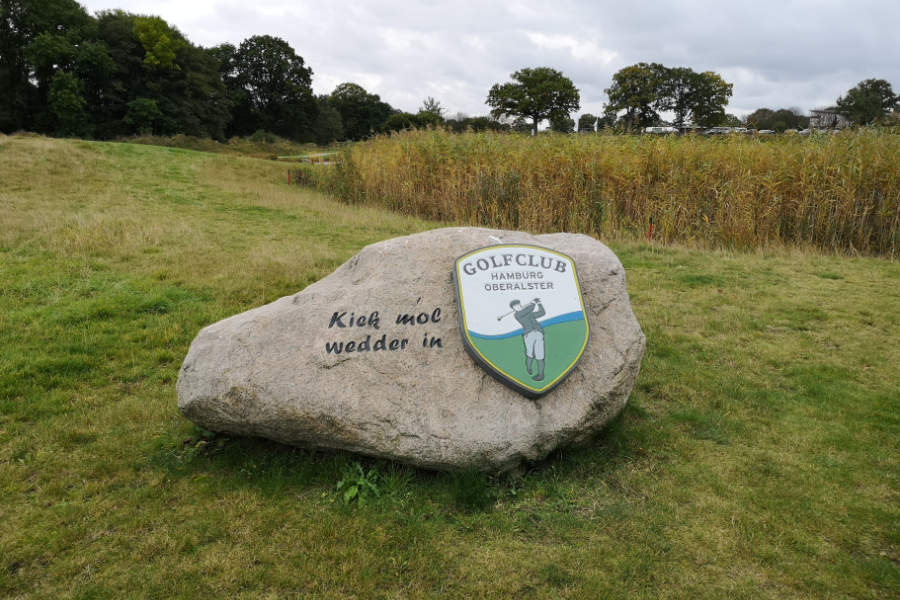 Ein großer Stein mit der Aufschrift "Kiek mol wedder in" und dem Logo des Golfclubs Hamburg-Oberalster