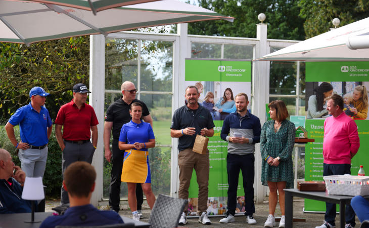 Golfer stehen vor Tafeln eines SOS Kinderdorfes