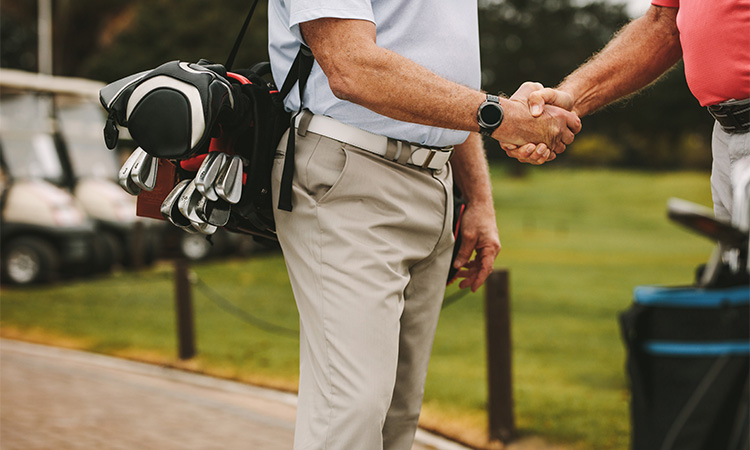 Ein Mann mit einer Golftasche um sich gibt einem anderen Mann die Hand