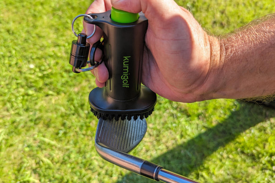 Eine Hand, die mit einer Wasserbürste einen Golfschläger reinigt