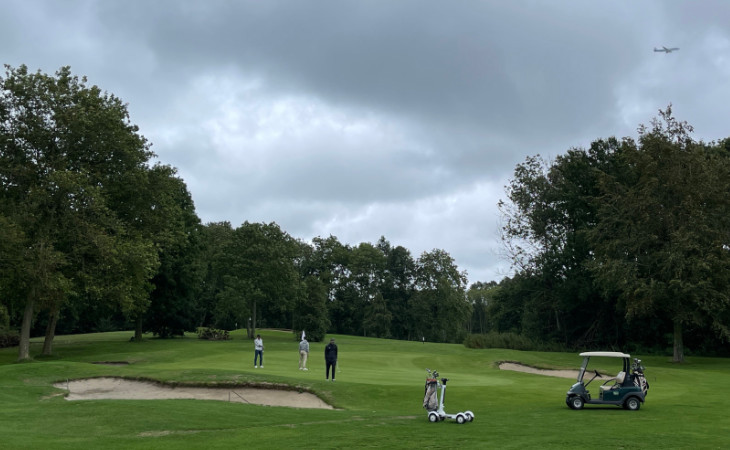 Einige Golfer auf einem Golfplatz, am Himmel ein Flugzeug