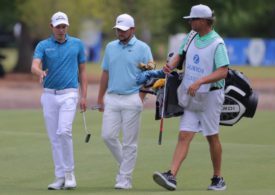 Zwei Golfer und ein Caddie gehen auf einem Golfplatz